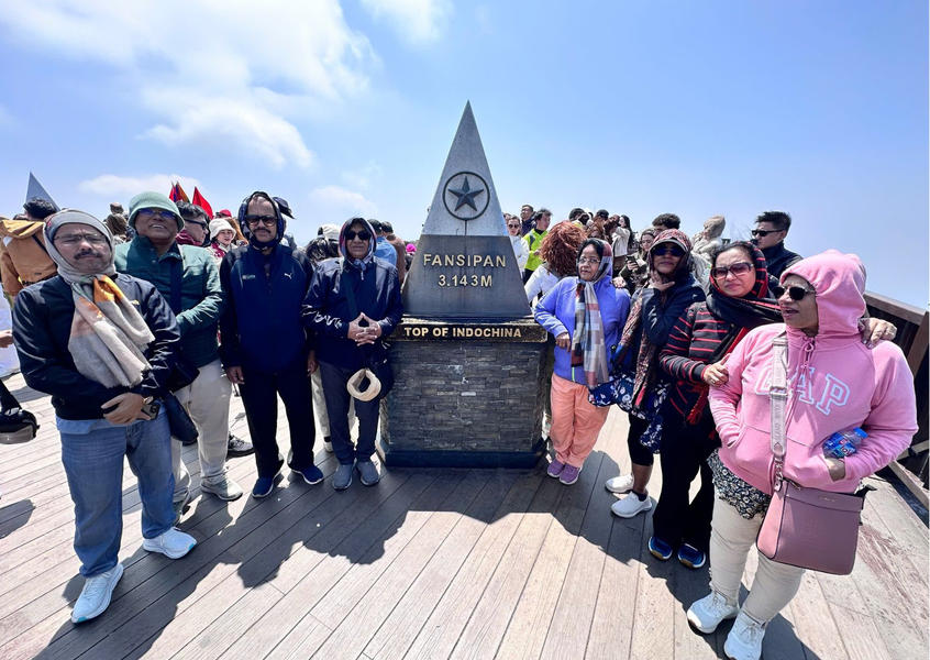 A group of travelers stands together by the Fansipan peak monument under a clear sky