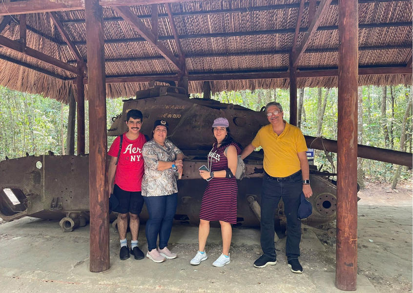 Four tourists stand next to a historic military tank at Cu Chi Tunnel