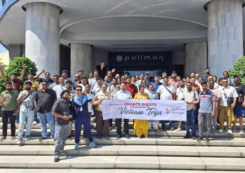 A big tour group holds a welcome banner while posing on the steps outside the Pullman hotel