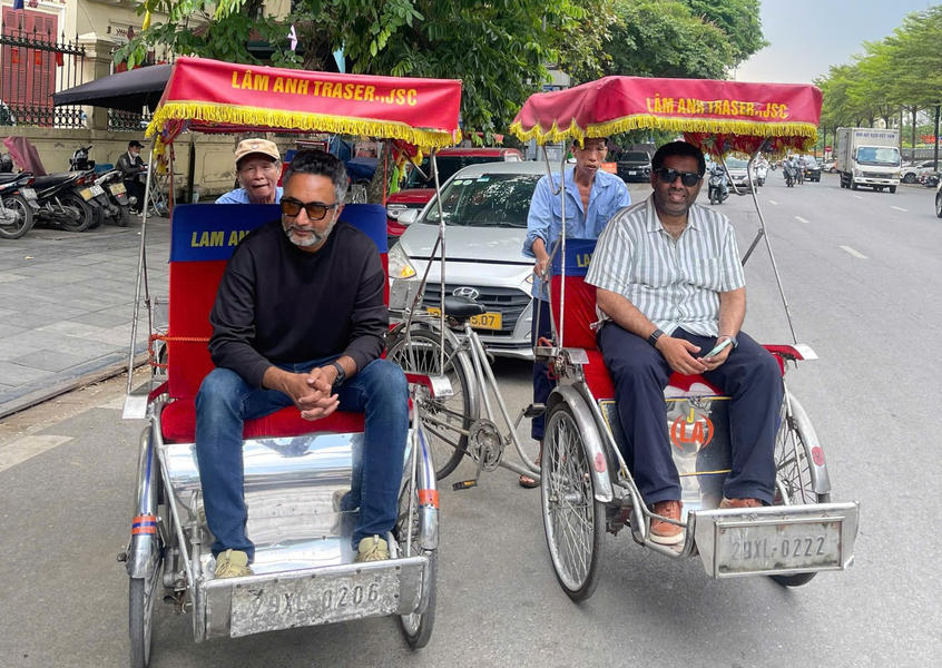 Two tourists riding traditional cyclo rickshaws on a street in Hanoi, Vietnam for a sightseeing tour