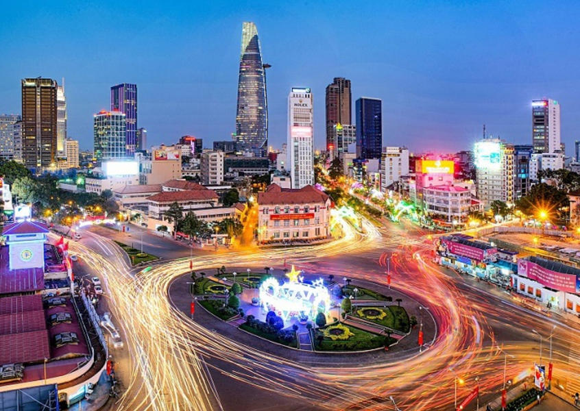 Ho Chi Minh City skyline at night with light trails from motorbikes circling a roundabout in District 1