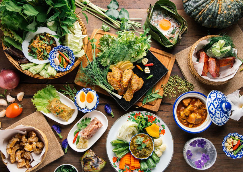 Authentic Thai cuisine spread with curries, fresh herbs, eggs, grilled meats, and traditional blue-and-white ceramic bowls