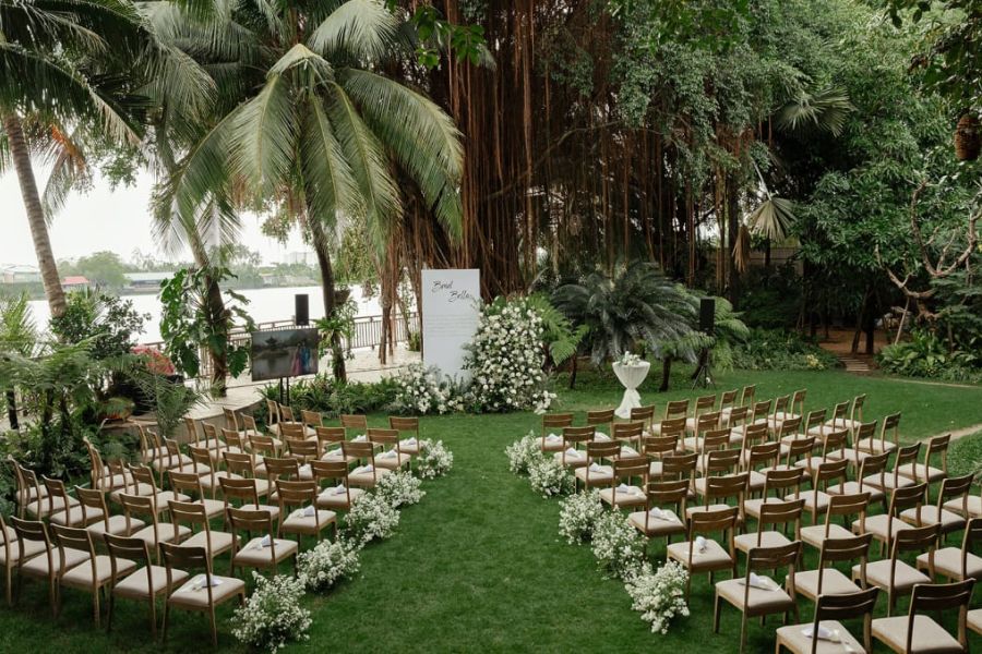 Garden aisle with wooden chairs under banyan tree by river
