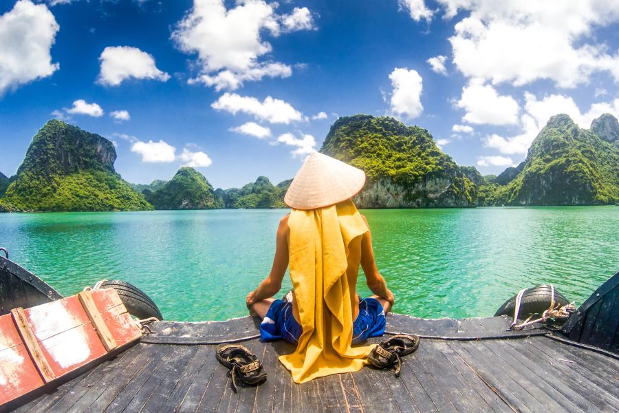 Traveler in traditional conical hat overlooking Ha Long Bay karst islands, Vietnam