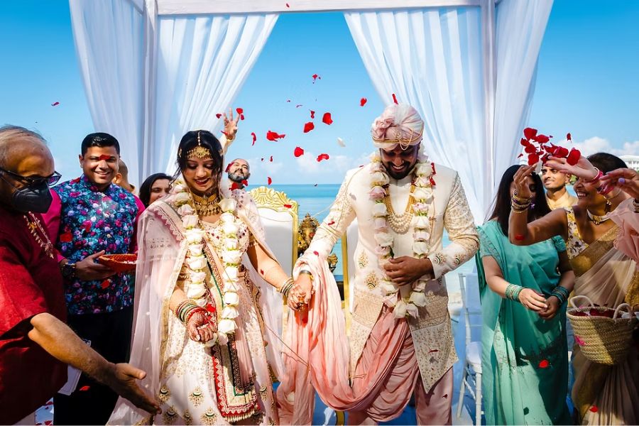 Indian bride and groom walk beachside amid rose petals