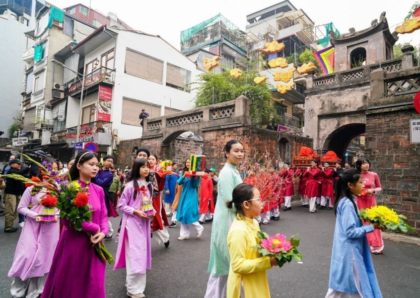 Women in ao dai carry flowers past ancient Hanoi gate, spring