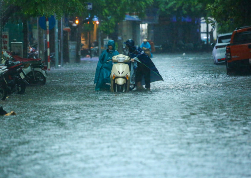 Flooded Hanoi street in monsoon rain, people push motorbike