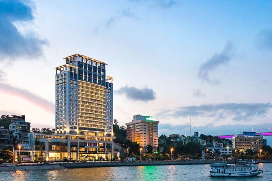 Modern high-rise waterfront hotel tower with glass facade overlooking Halong Bay harbor at dusk