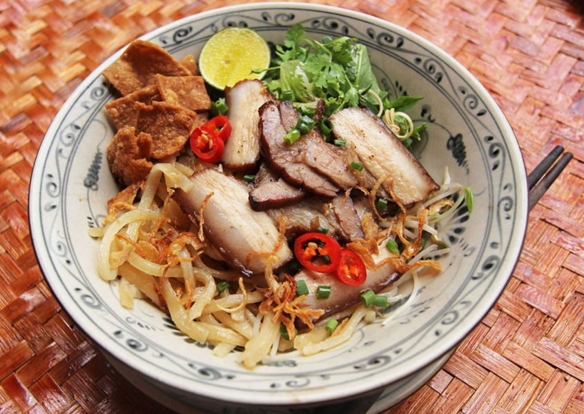 Bowl of Cao Lau noodles with pork slices and herbs in Hoi An