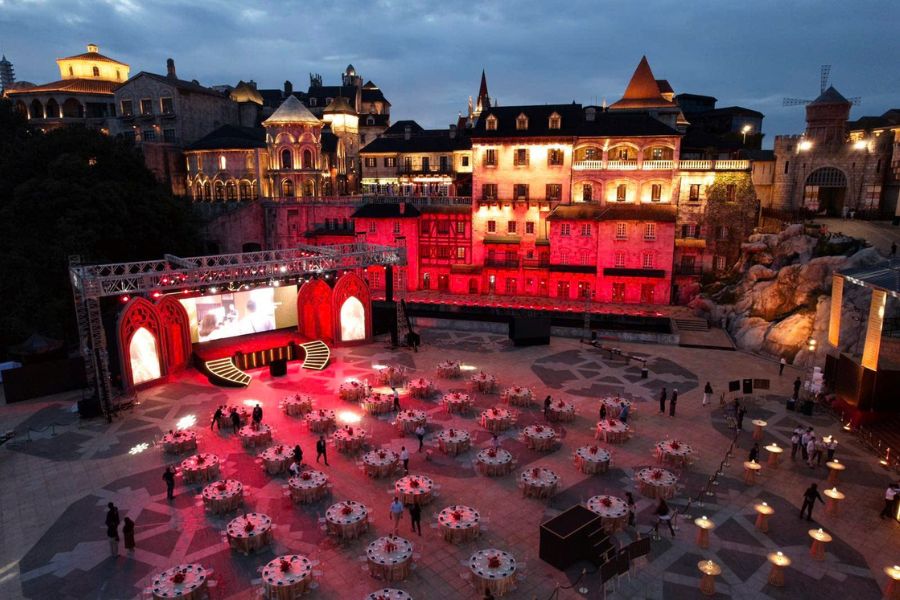 Outdoor gala dinner setup at a European-style themed village near Da Nang, lit up at dusk